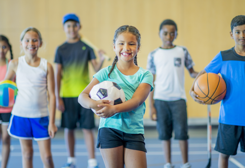 A group of children in a gymnasium holding sports equipment