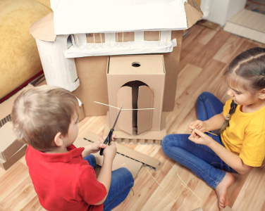 Two children building a cardboard fort. 