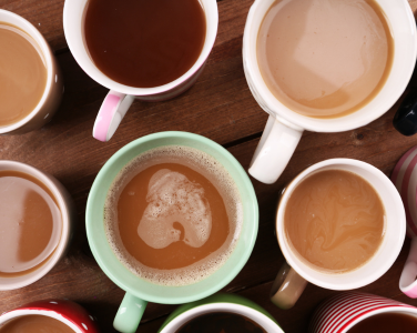 Various coffee mugs filled with coffee on a wooden table.