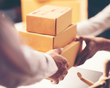 Two people exchanging stacked cardboard boxes.