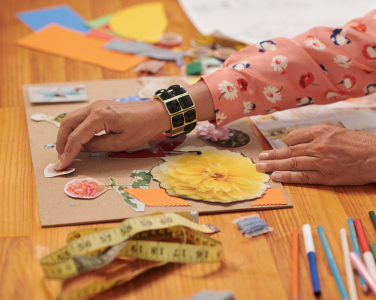 Person's hands crafting with paper and art supplies.