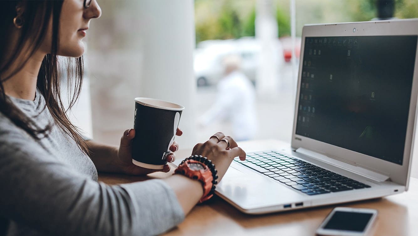 A person seated at a keyboard, holding a steaming cup of coffee in one hand