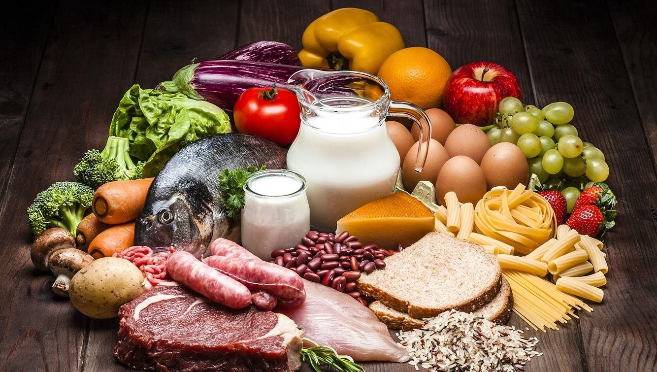 The image features a vibrant assortment of fish, milk, cheese, vegetables, bread, eggs and fresh fruits, beautifully arranged to highlit variety and freshness.