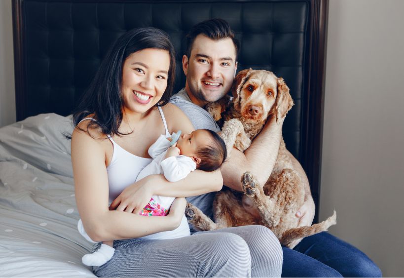 young family with baby and dog sitting on bed