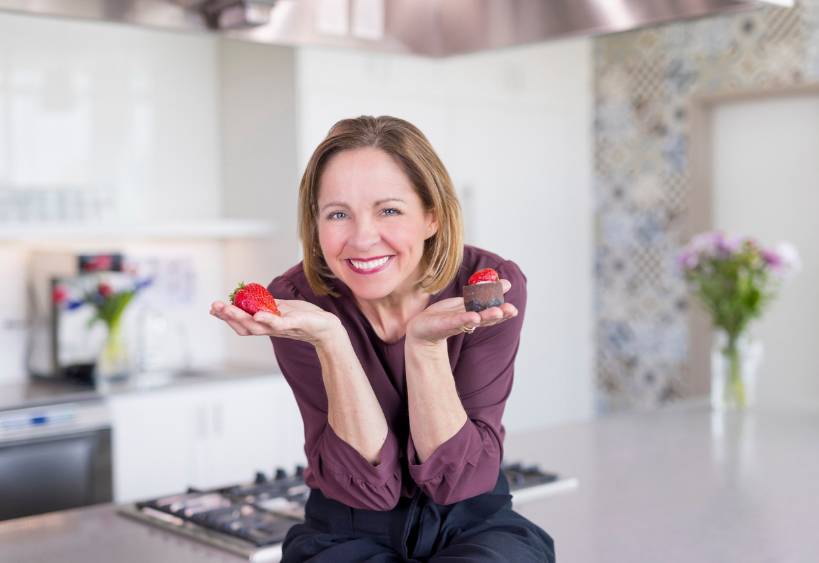 Andrea Holwegner holding a chocolate in one hand and a strawberry in the other
