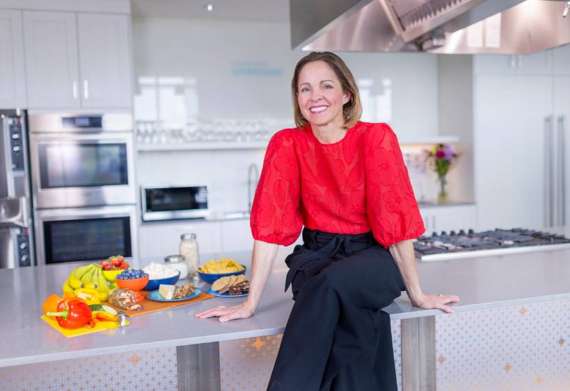 Andrea Holwegner sitting on kitchen counter with assortment of foods