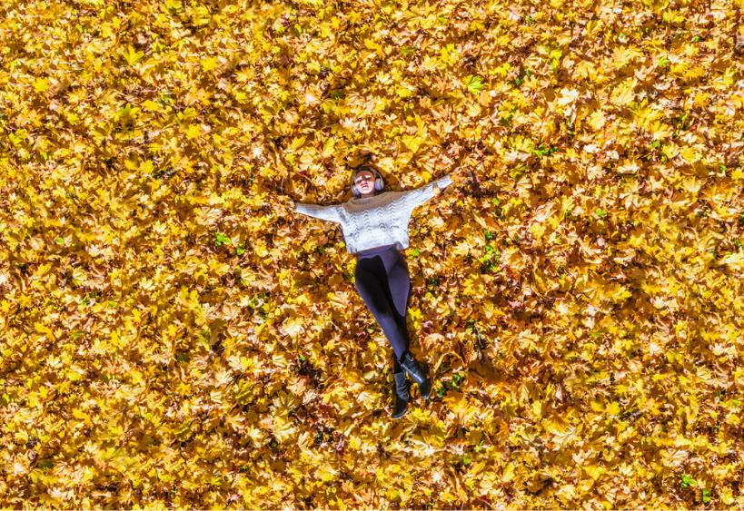 Young woman in headphones listening music lying and relaxing on the autumn maple leaves in the park