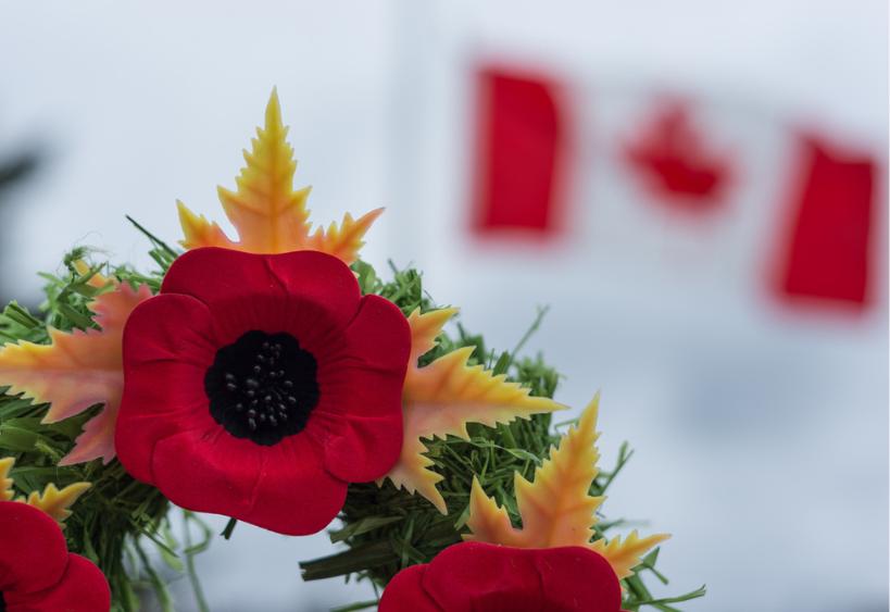 A Remembrance Day wreath surrounded by Poppies and a background of a Canadian Flag