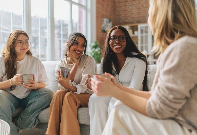 Four women sitting on a couch drinking warm drinks