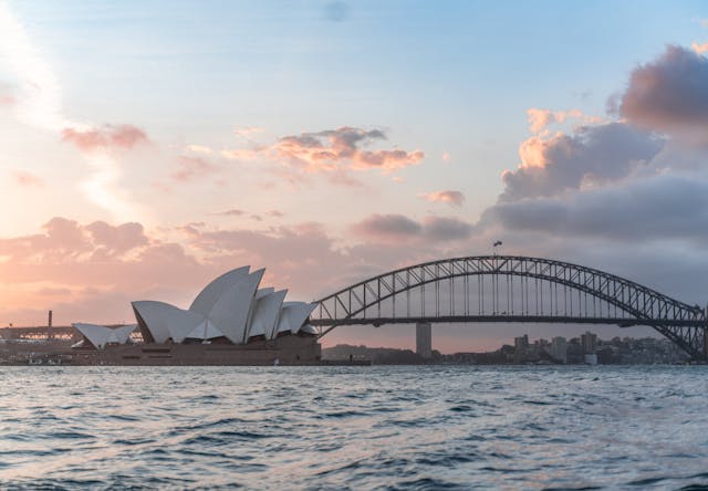 Scenic view of Sydney Opera House and Harbour Bridge during sunset over the water.