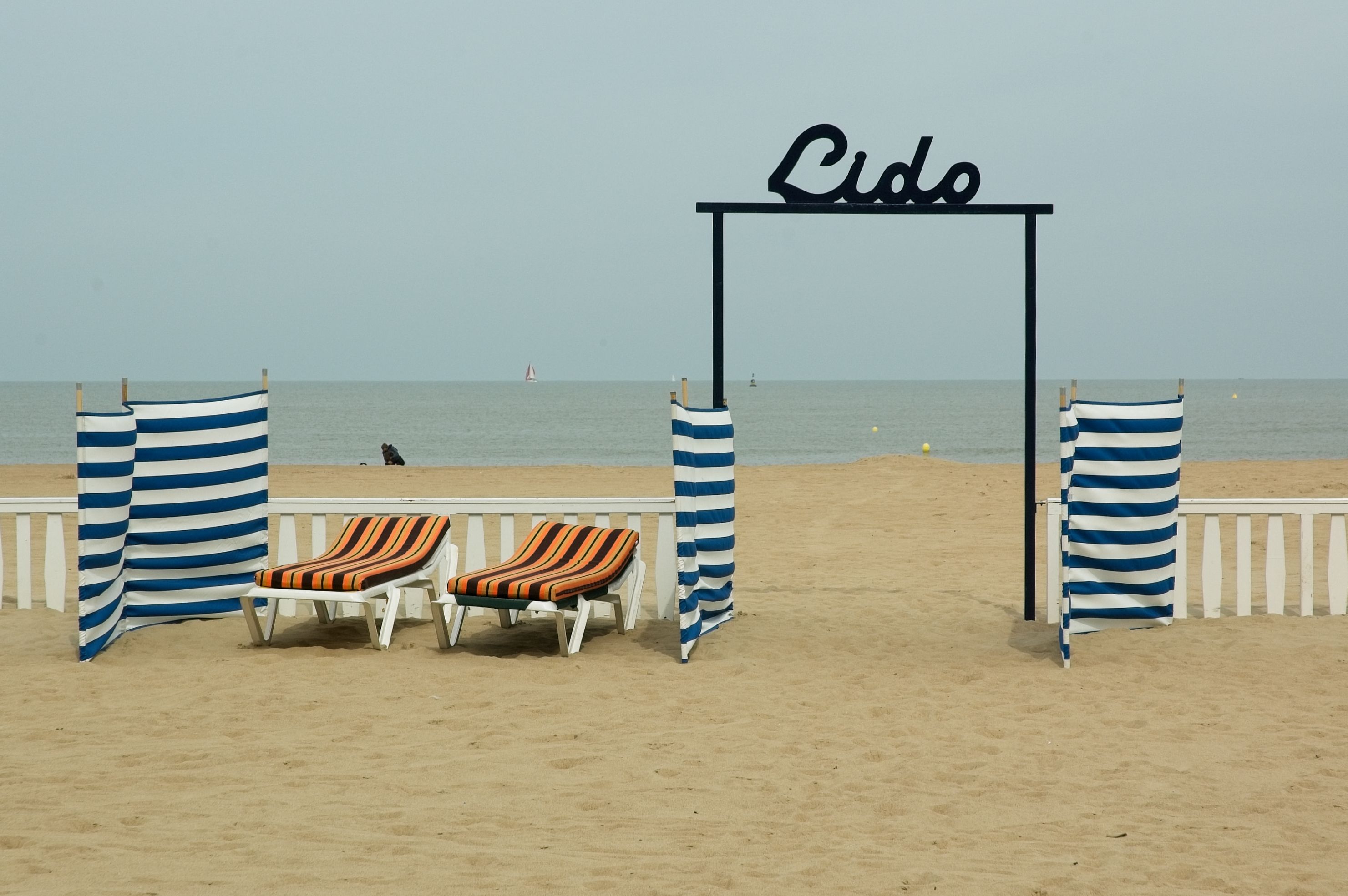 Relaxing beach scene with loungers, striped canopies, and a view of the sea under a Lido gate.