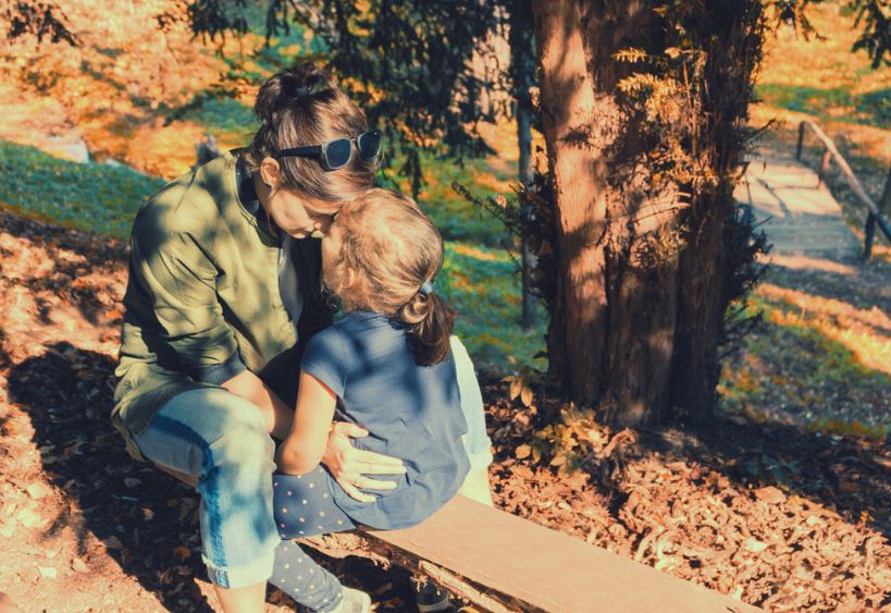 woman and girl sitting on a bench outside with foreheads pressed together