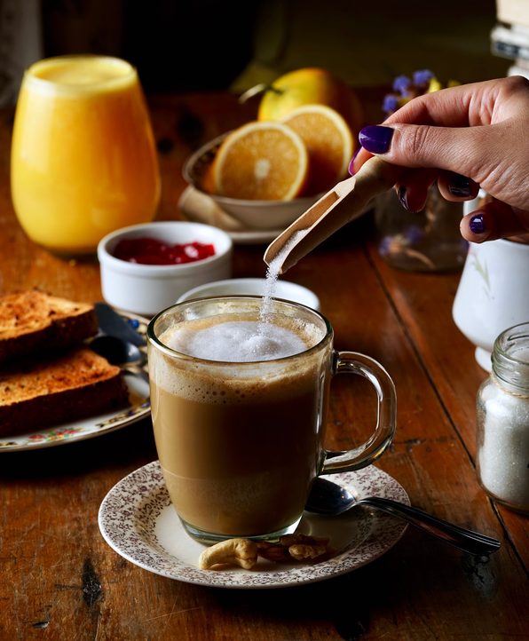 hand pouring sugar into a coffee sitting on a table