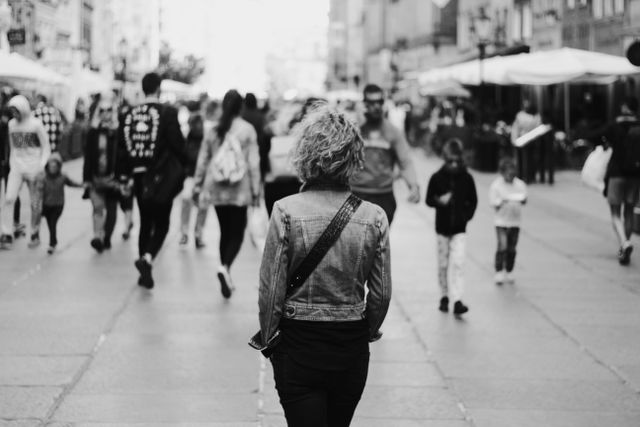 Monochrome photo of a busy urban street with people walking, focusing on a woman from behind.