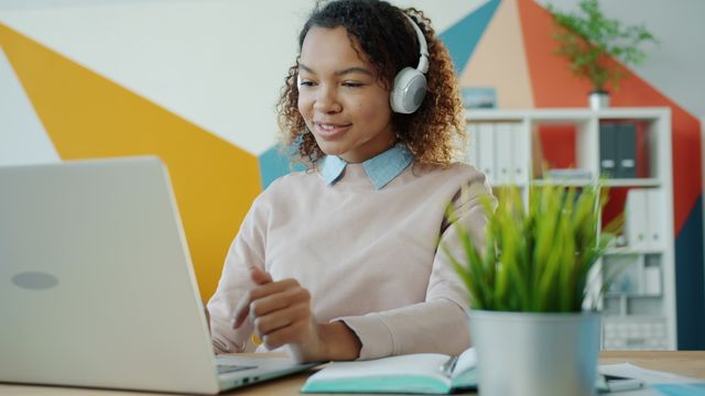 Young woman using laptop with headphones in a modern office setting.