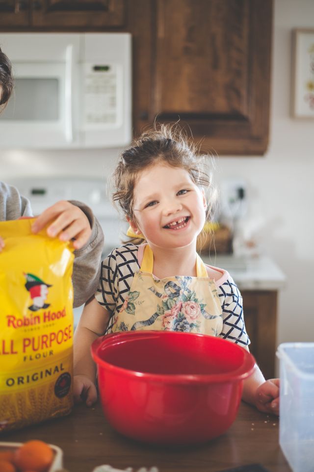 smiling girl wearing an apron standing behind a red bowl sitting on the counter