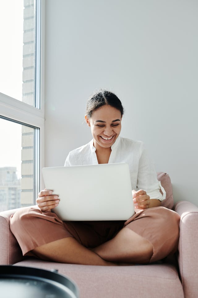 person sitting in a chair, smiling at their laptop