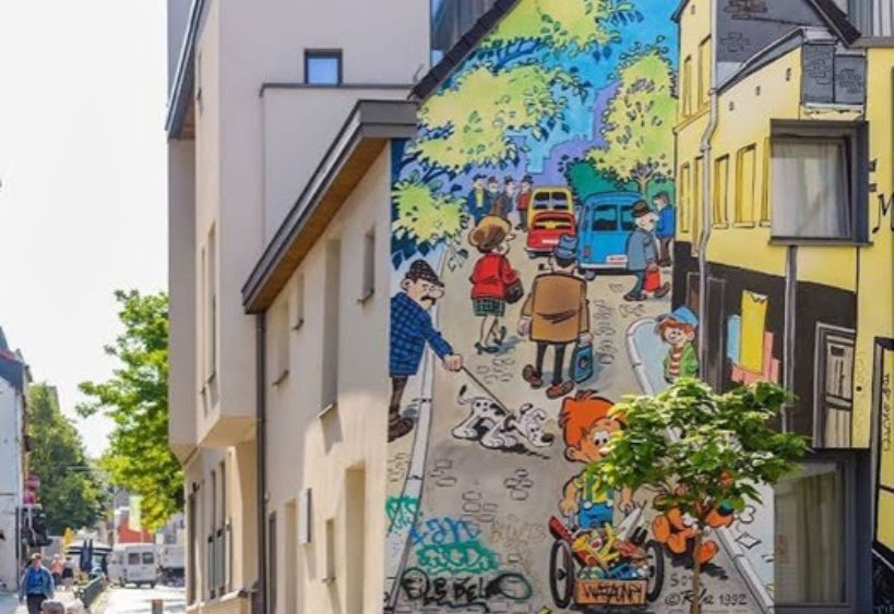 A colourful comic-style mural decorates the side of a building along a city street.
