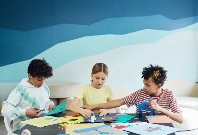 three kids doing crafts on a table