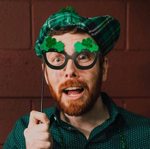 man with St. Patrick's day clothing and eye glasses prop looking at camera with surprised expression