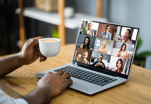 person holding a cup of coffee while looking at online meet on a laptop