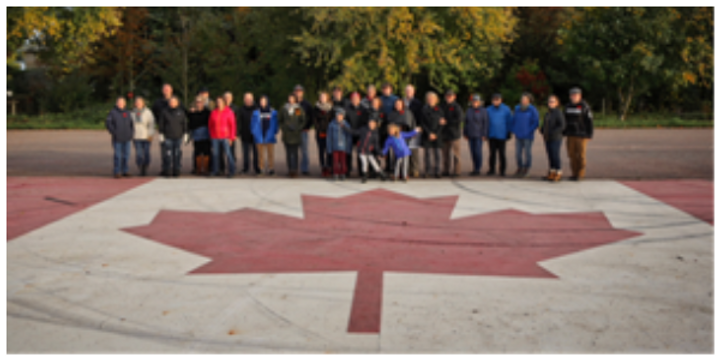group of people standing behind a canadian flag painted on the ground