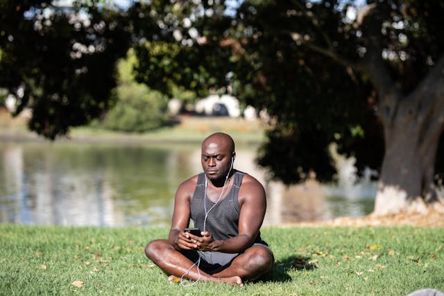 Person in Gray Tank Top Using Cellphone While Sitting on Grass