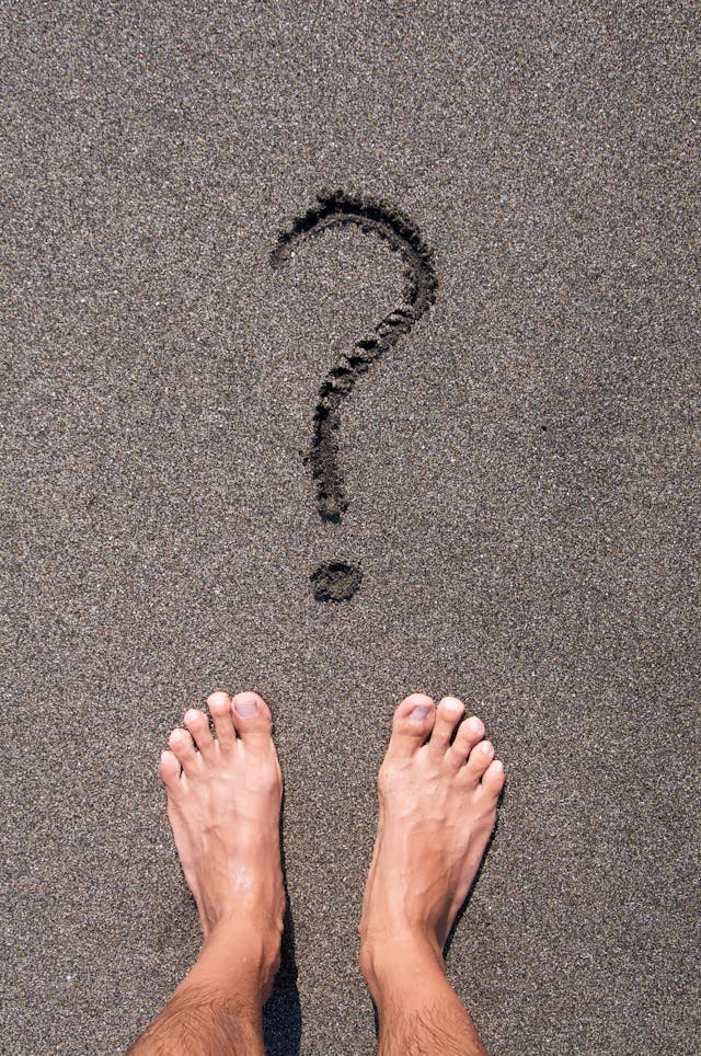 Person Standing on Black Sand Beach in Front of Question Mark
