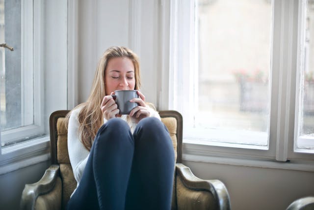 woman with her eyes closed curled up in a chair with a mug