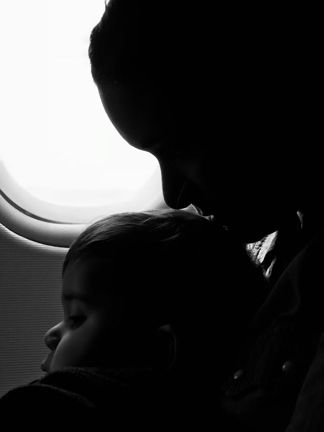 greyscale photo of woman with baby on lap on a plane