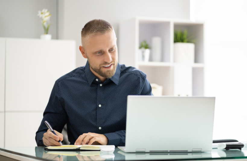 man with computer and writing in notebook