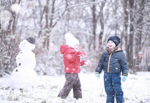 preschool boy and girl in snow gear playing in the snow and building a snow man