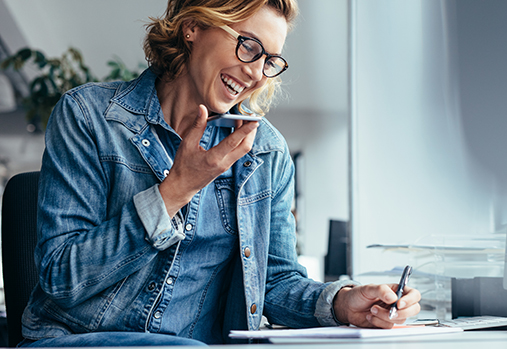 Young female executive working in office. Smiling young businesswoman talking on cellphone and writing notes