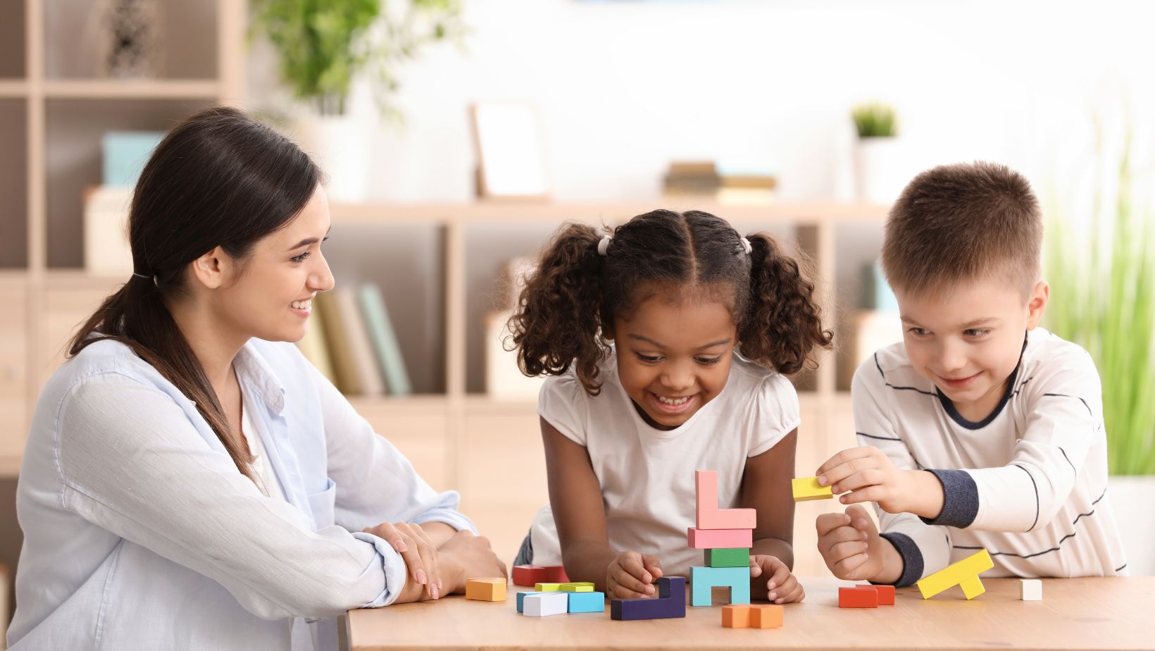 caregiver playing with two children at a table
