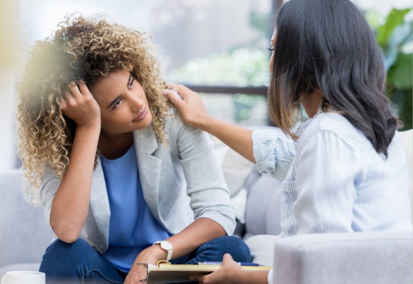 two women sitting and one supporting the other