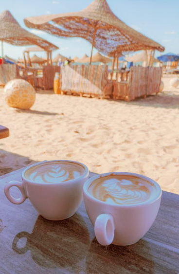Two cups of coffee sitting on a table next to a sandy beach