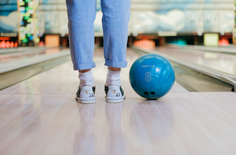 A person standing at the end of a bowling lane with a blue bowling ball next to them