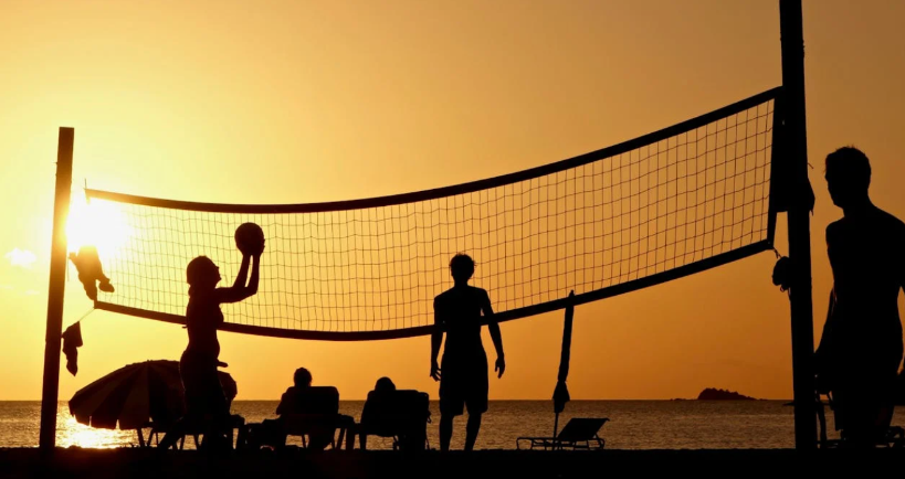 People playing beach volleyball at sunset