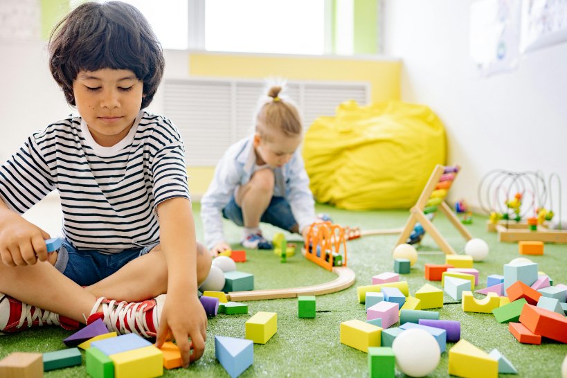 Two children playing with building blocks and a wooden train